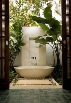 a bathtub in the middle of a room with plants on either side and an open door leading to another area