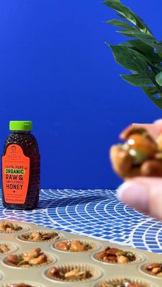 a hand holding a jar of organic honey next to muffins on a table