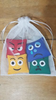 three small bags with faces on them sitting on a wooden floor next to a string bag