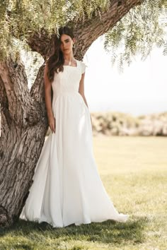 a woman standing next to a tree wearing a white dress