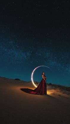 a woman in a long red dress is standing on the sand with her arms around an object