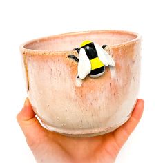 a hand holding a ceramic bowl with a yellow and black bee decoration on the side