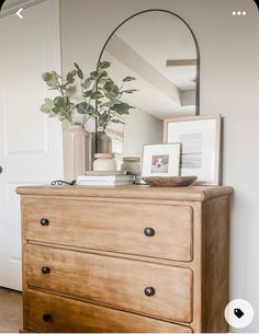 a dresser with a mirror, plant and pictures on it