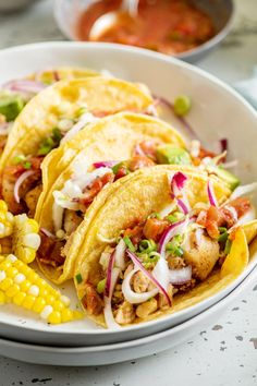 a white plate topped with three tacos and corn