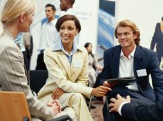 three people sitting in chairs talking to each other at a business meeting with others looking on