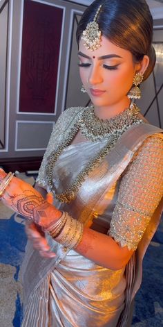 a woman in a silver sari is looking at her cell phone while wearing jewelry