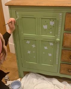 a woman painting a green cabinet with flowers on it