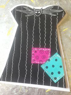 a dress made out of black paper with blue and pink patches on the front, sitting on top of a piece of cardboard