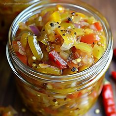 a glass jar filled with pickled vegetables on top of a table next to red peppers