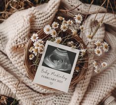 a baby announcement with daisies in a wicker basket on top of a blanket