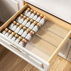 an open drawer filled with lots of bottles on top of a wooden floor next to a white refrigerator