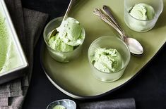 three bowls filled with green ice cream next to two spoons on a plate,