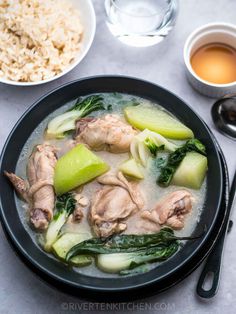 a black bowl filled with meat and vegetables next to rice