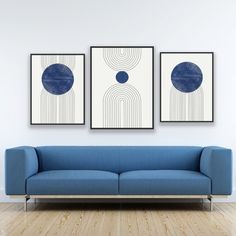 two blue couches sitting in front of a white wall with three paintings on it