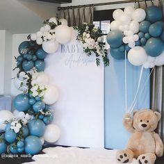 a teddy bear sitting on top of a bed next to balloons and a baby shower sign