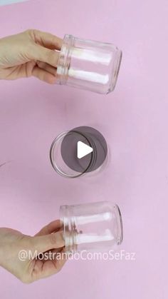 two hands are holding empty glass jars on a pink surface, one is open and the other is closed