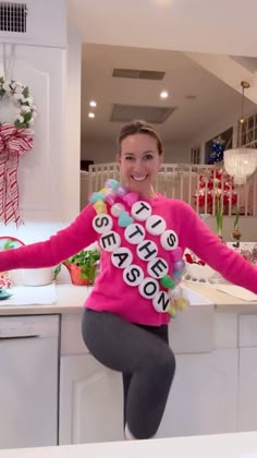 a woman in a pink sweater is standing on a kitchen counter with her arms out