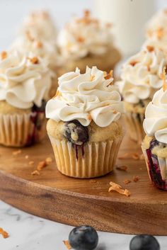 cupcakes with white frosting and blueberries on a wooden board