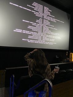 a woman sitting in front of a projector screen holding a drink and looking at the screen