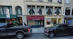 two pickup trucks parked in front of a building on a city street with people walking down the sidewalk