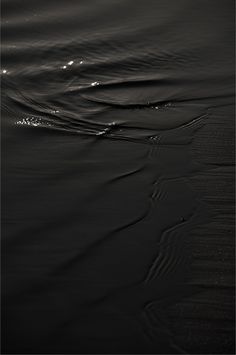 a black and white photo of water with ripples on the sand at night time