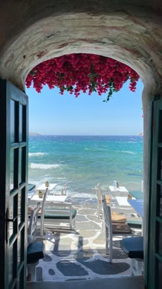 an open door leading to the beach with flowers hanging from it's roof and water in the background