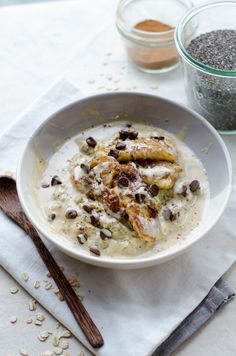 a white bowl filled with food next to two spoons on top of a table