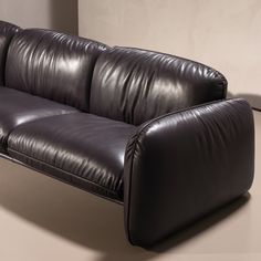 a black leather couch sitting on top of a white floor next to a wall and lamp