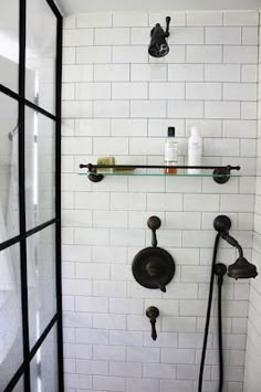 a shower with black fixtures and white tiled walls, along with shelves on the wall