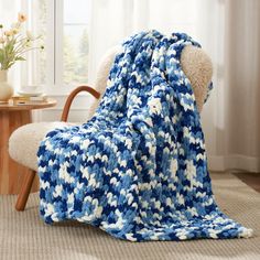 a blue and white crocheted blanket sitting on top of a wooden chair next to a window