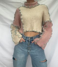 a woman wearing ripped jeans and a sweater with ruffles on the sleeves is standing in front of a white backdrop