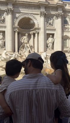 a group of people standing in front of a building with statues on the side of it