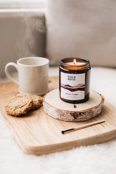 a candle sitting on top of a wooden tray next to a cup and cookie slice