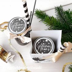 two boxes with christmas decorations and ribbons on the table next to some pine branches, one is black and white