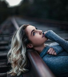 a woman laying down on train tracks with her hand under her chin and looking off to the side