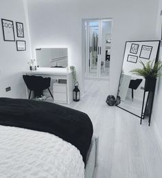 a bedroom with white walls and flooring has black accents on the bed, mirror, desk, and dresser