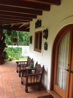 an outside patio with wooden chairs and potted plants on the wall, next to a door