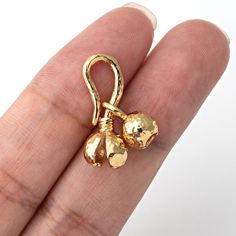 a hand holding a gold charm with two bells on it's back end,