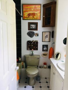 a white toilet sitting inside of a bathroom next to a sink and window with pictures on the wall