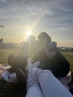 two people sitting on a blanket in front of the sun with their arms around each other