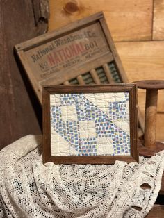 an old wooden chair with a quilt on it and a framed picture in the middle