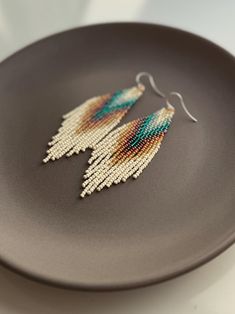 a pair of beaded earrings sitting on top of a black plate next to a white wall