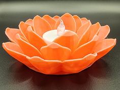 an orange flower sitting on top of a black table next to a white candle holder