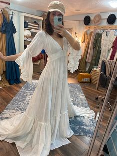 a woman taking a selfie in front of a mirror wearing a white dress and hat