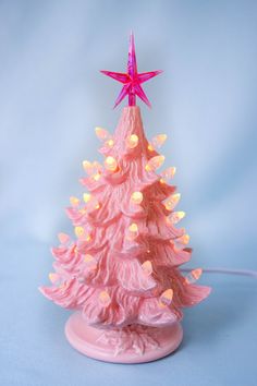 a pink ceramic christmas tree with lights on it's base and a star on top