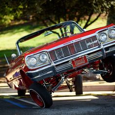 an old red car is parked in a parking lot with the hood down and it's front end lifted up