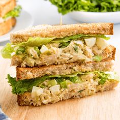 a sandwich cut in half sitting on top of a wooden cutting board with lettuce