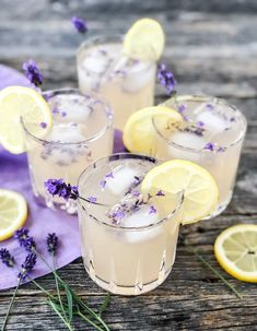 three glasses filled with lavender lemonade on top of a wooden table next to sliced lemons