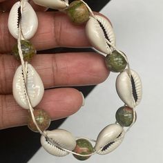 a hand holding a bracelet with shells on it