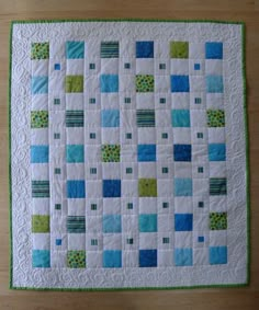 a quilted wall hanging on the side of a wooden floor with green and blue squares